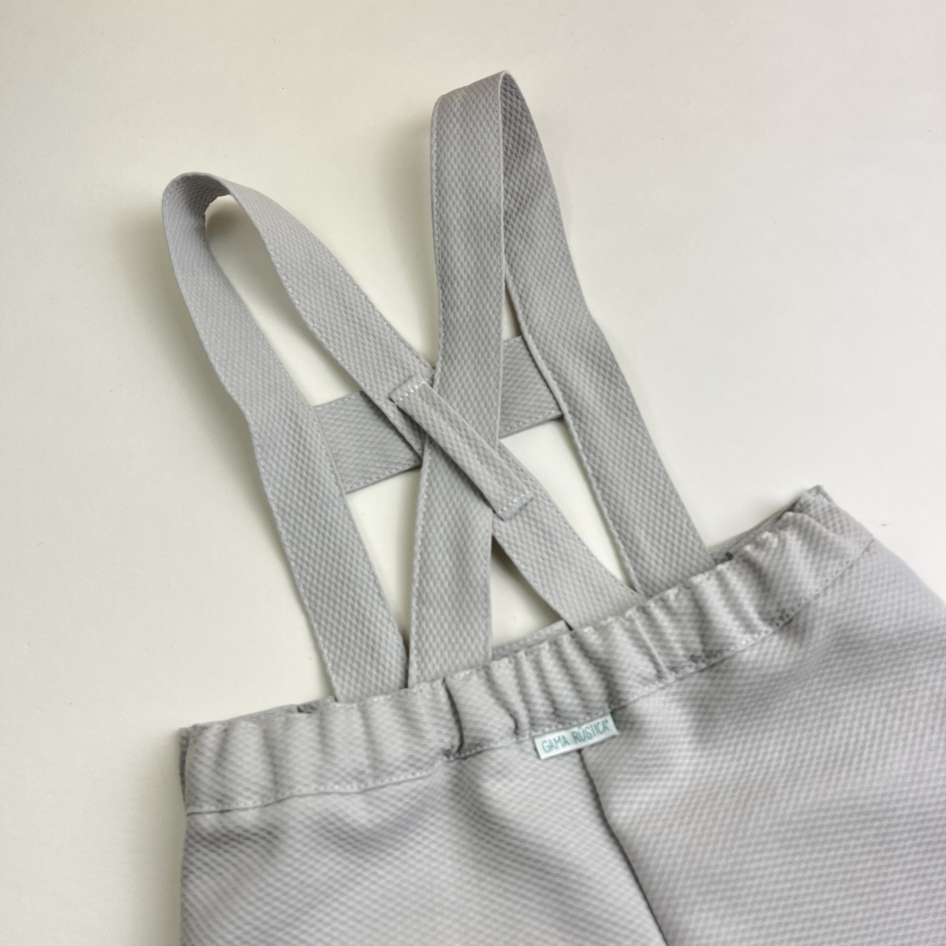 Calças cinza claras com alças cruzadas em fundo branco