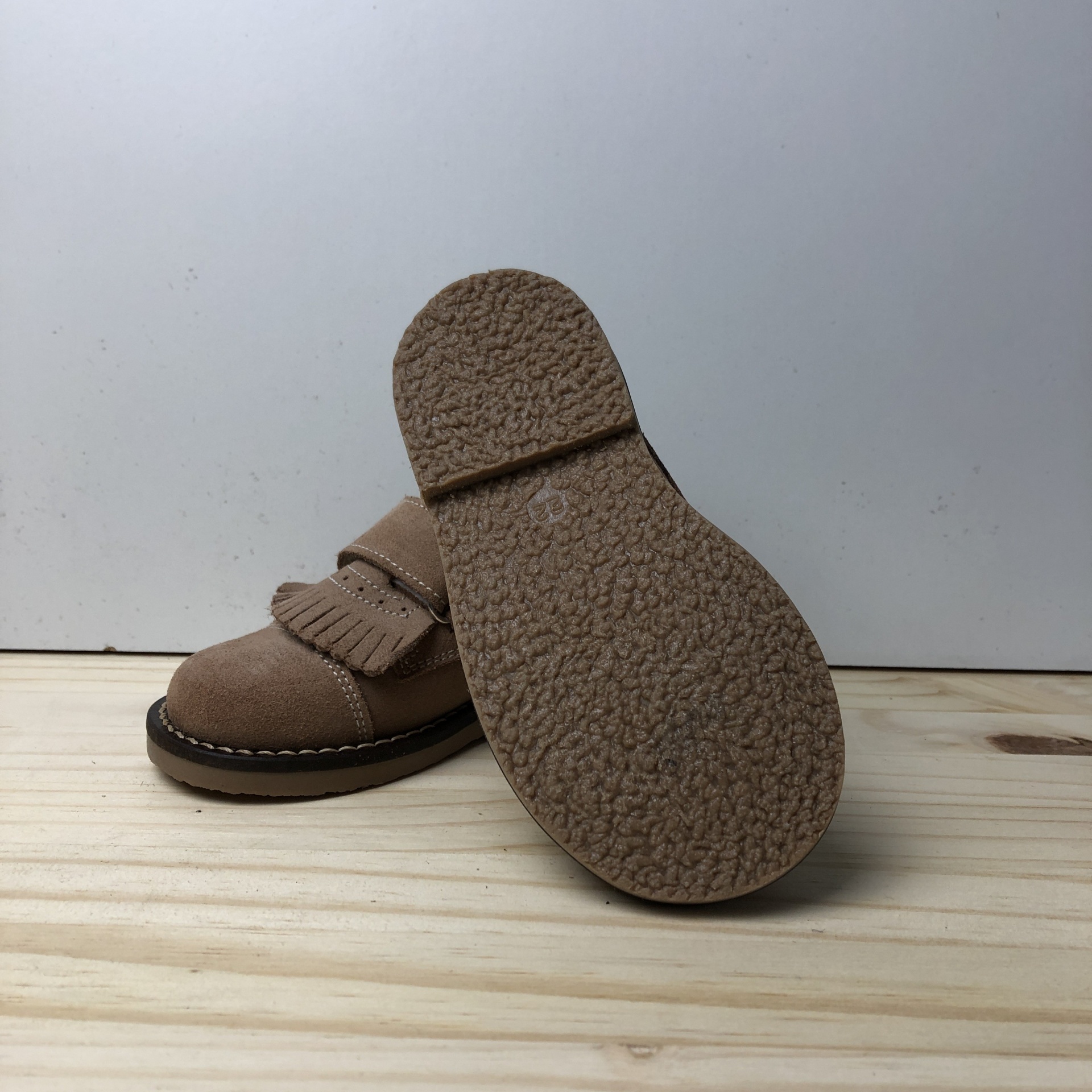 Sapato infantil bege em camurça com sola texturizada e detalhes de franjas.