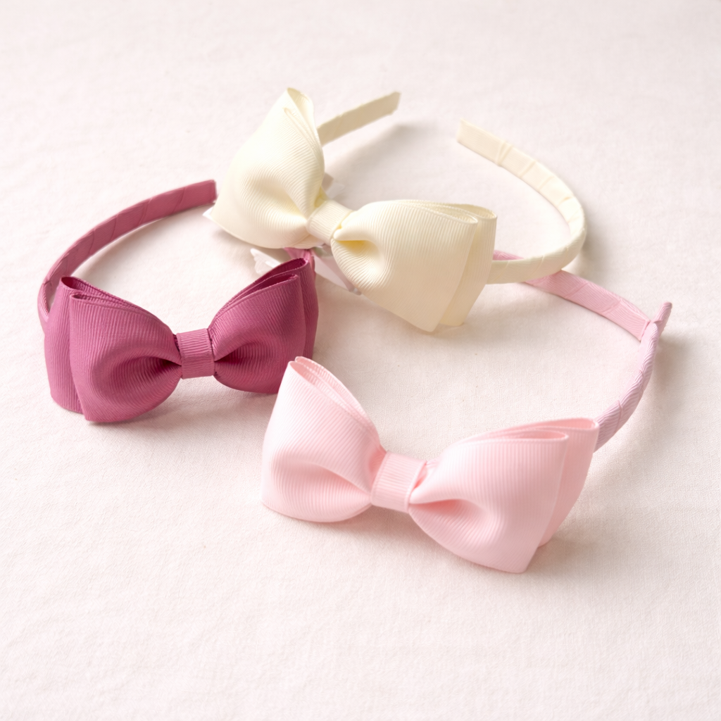 Três tiaras com grandes laços de tecido em creme, rosa claro e rosa escuro em tecido com textura riscada