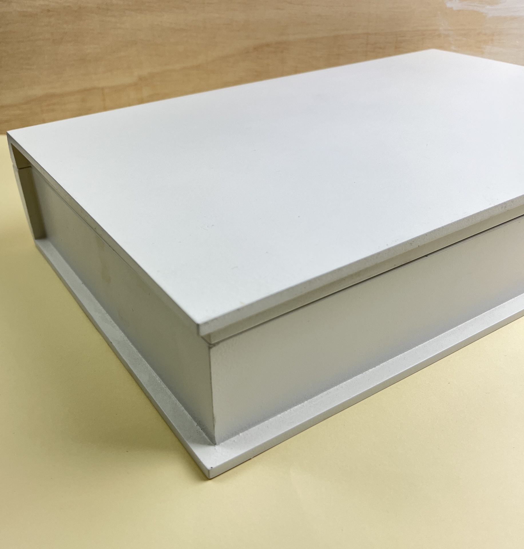 Caixa branca retangular com tampa e base em madeira