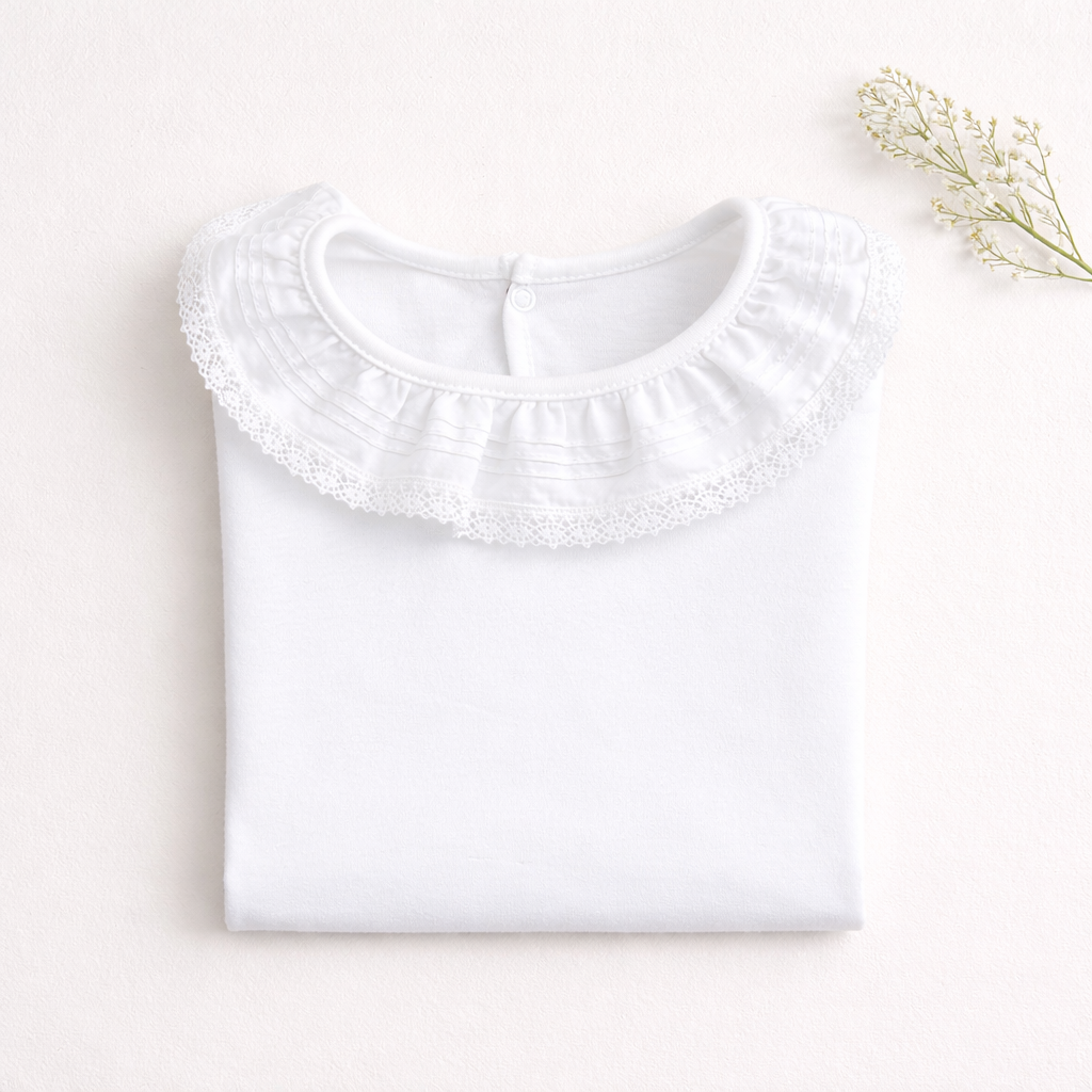 Camisa branca dobrada com gola com renda e botão atrás sobre superfície clara com ramo seco