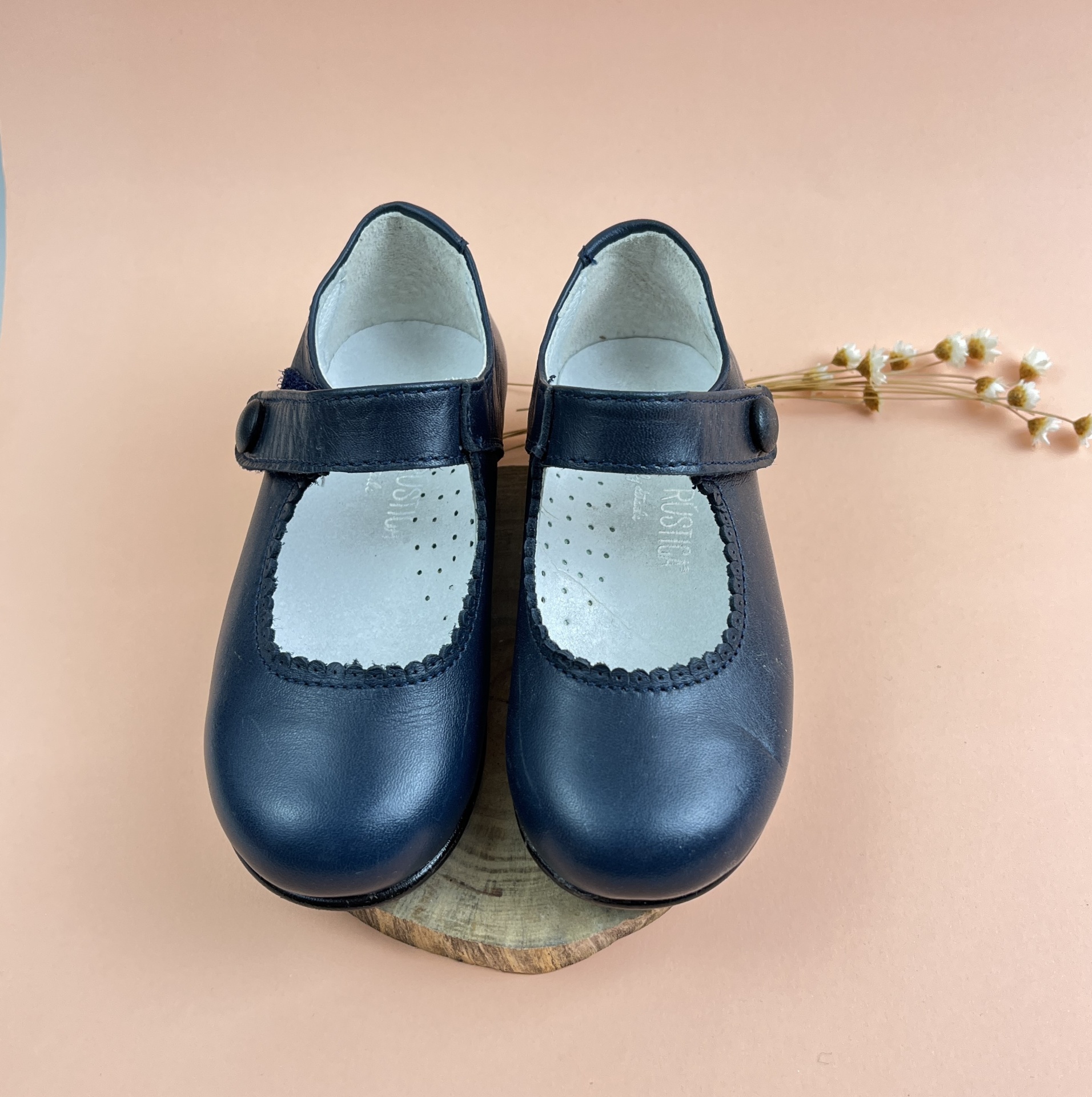 Sapatos infantis pretos em pele com fecho de velcro sobre suporte de madeira