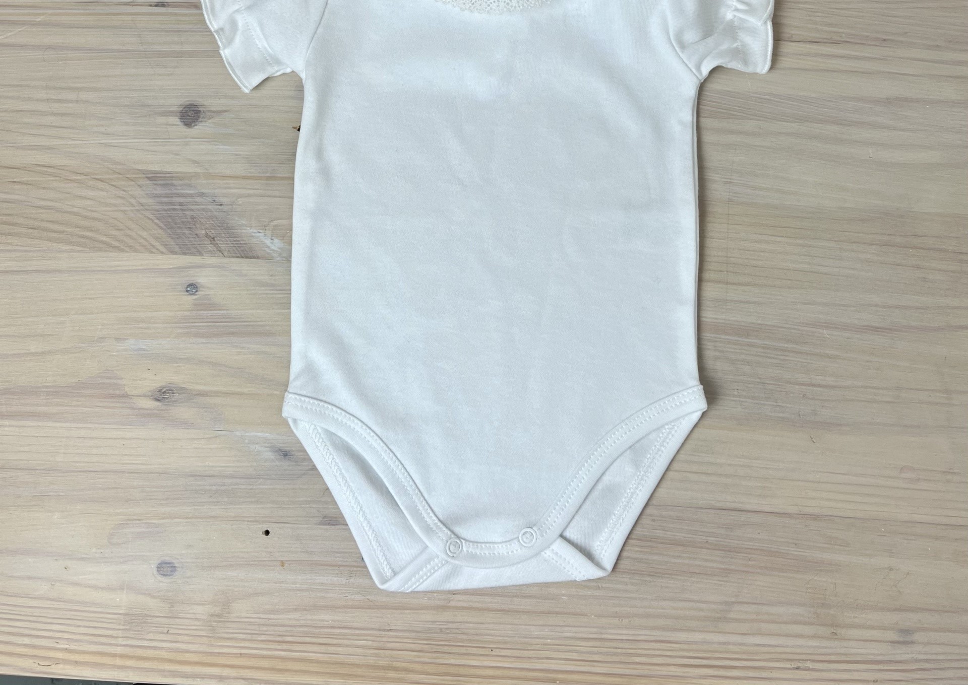 Body branco de manga curta com gola rendada sobre mesa de madeira clara