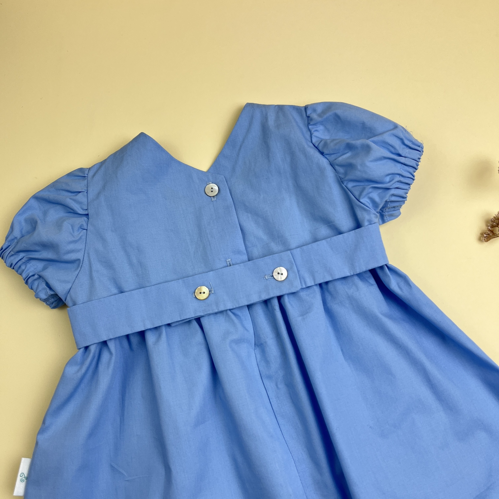 Vestido infantil azul claro com botões brancos na parte de trás