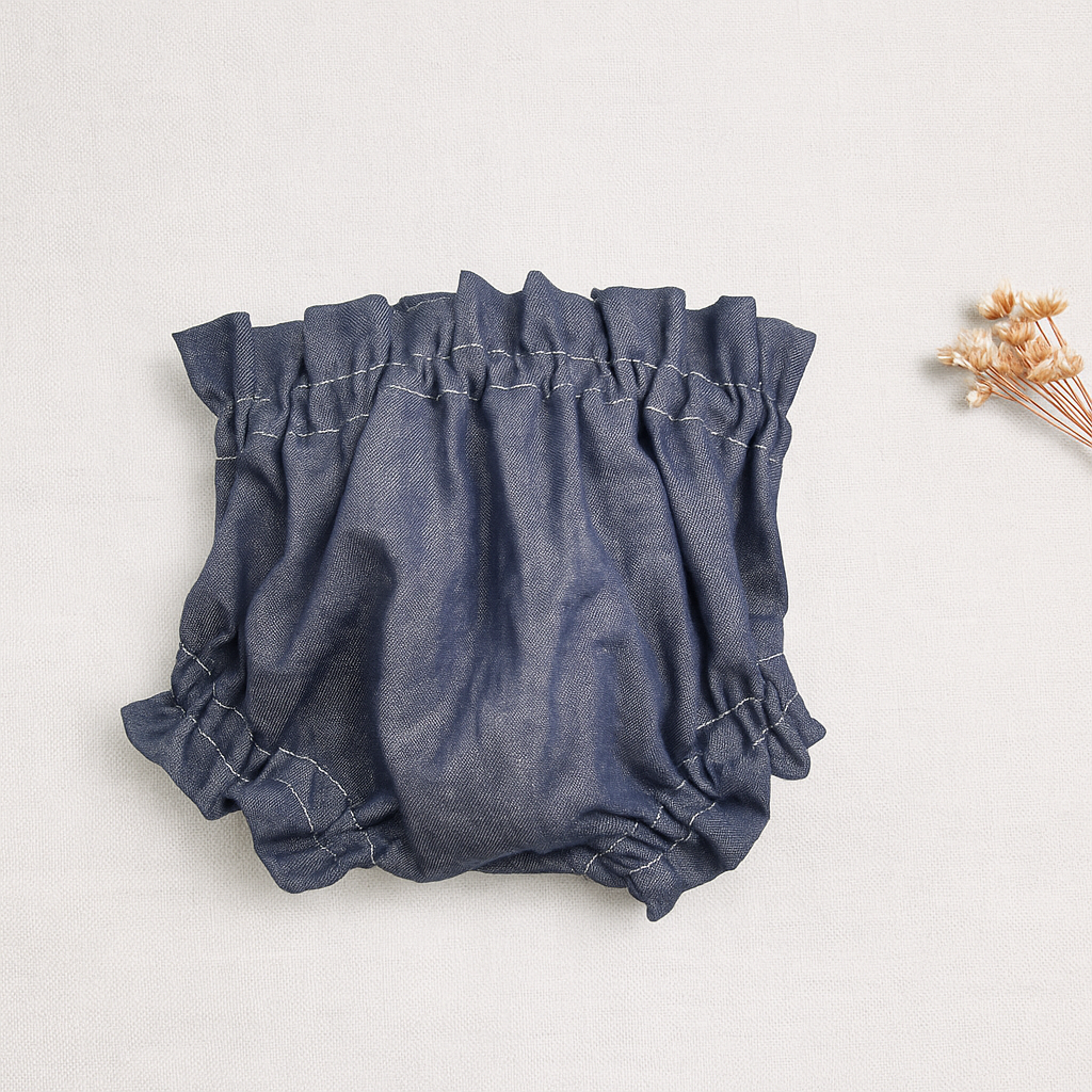 Cuecas de bebé azul escuro com costuras visíveis colocadas sobre fundo claro com flores secas ao lado