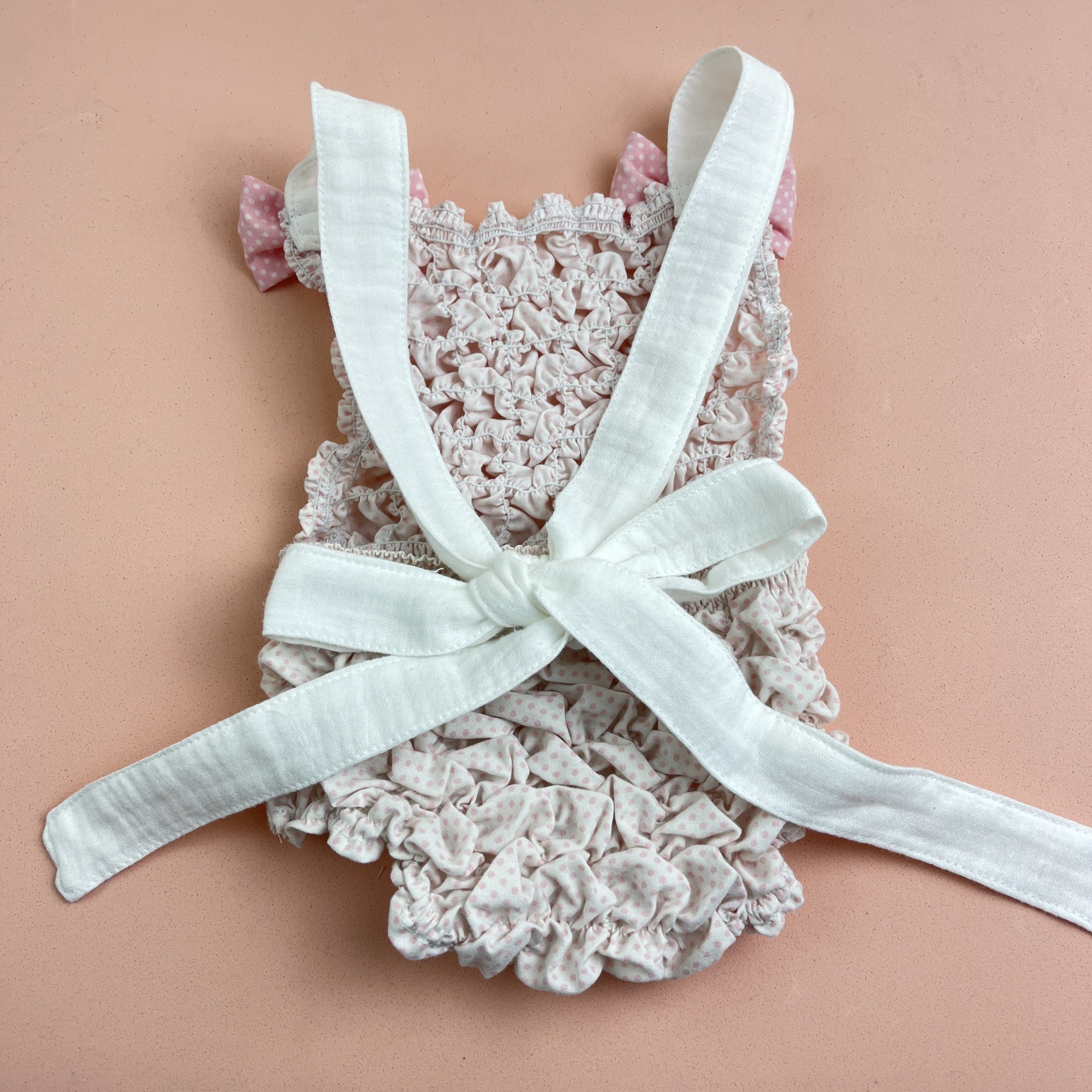 Roupa de bebé creme com detalhes rosas e fita branca sobre fundo rosa