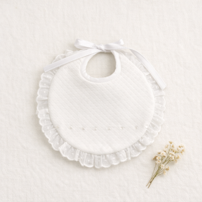 Babete branco acolchoado com renda e laço sobre tecido branco