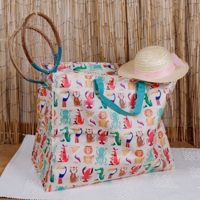 Saco com padrão de animais, chapéu de palha e raquetes ao lado, em ambiente com tapete branco e fundo de cana seca