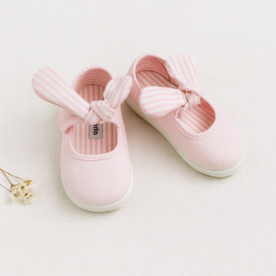 Sapatilhas infantis cor-de-rosa com fita às riscas e sola branca sobre superfície branca