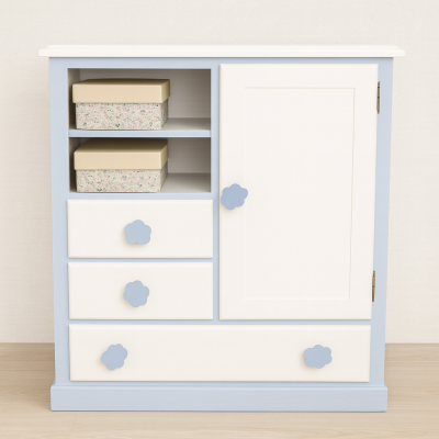 Móvel branco e azul claro com gavetas e porta, puxadores em forma de nuvem azul, duas caixas decorativas nas prateleiras abertas.