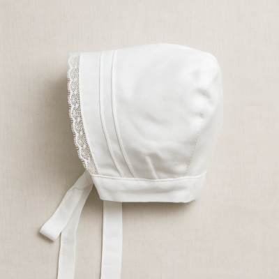 Touca ou capuz branco com renda e fitas sobre fundo bege