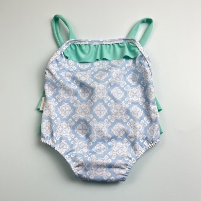 Fato de banho de criança azul e verde com padrão branco sobre fundo cinza claro