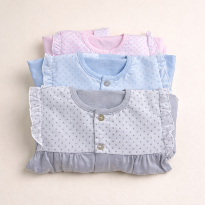 Três pijamas de bebé com padrão de pontos e folhos, em cinza, azul e rosa.