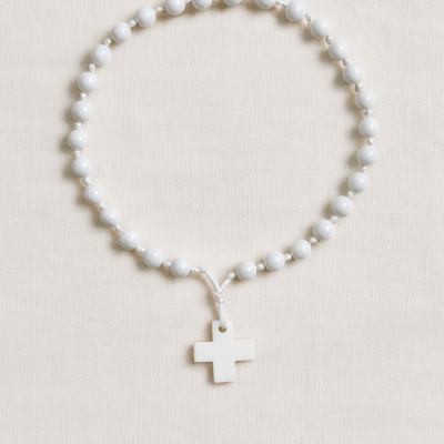 Terço branco com contas e cruz pendurada sobre tecido bege claro