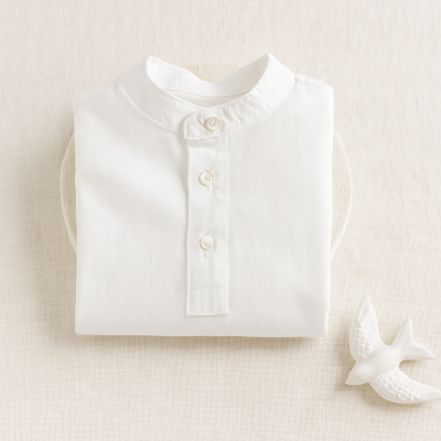 Camisola branca de algodão com gola mandarim e botões dobrada sobre tecido claro com figura decorativa de pássaro