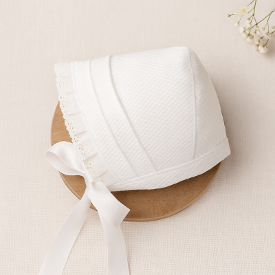Chapéu branco de bebé com fita de cetim e renda, em fundo claro com prato de madeira.