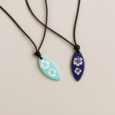 Dois colares com pendentes em forma de folha decorados com flores, um azul claro e outro azul escuro, com cordão castanho escuro.