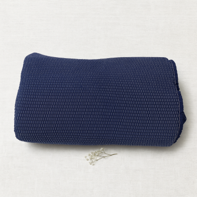 Manta azul escura dobrada com padrão texturizado e pequena flor branca ao lado