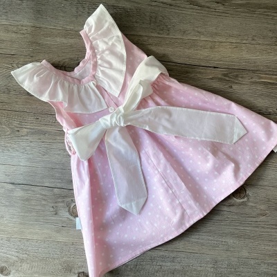 Vestido rosa com bolinhas brancas e gola e laço brancos sobre madeira clara