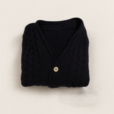 Camisola de malha preta com padrão tranças e botão, dobrada sobre fundo bege