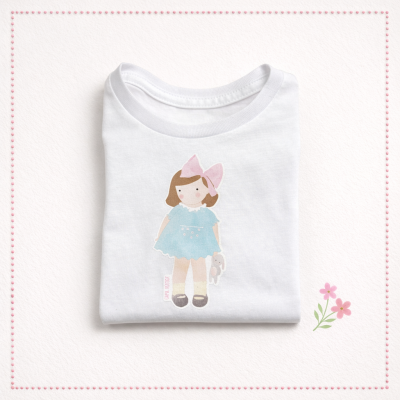 Camisola branca para criança com desenho de boneca e laço rosa.