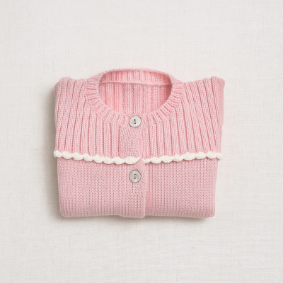 Cardigã infantil cor-de-rosa com detalhes brancos e botões, dobrado sobre superfície clara