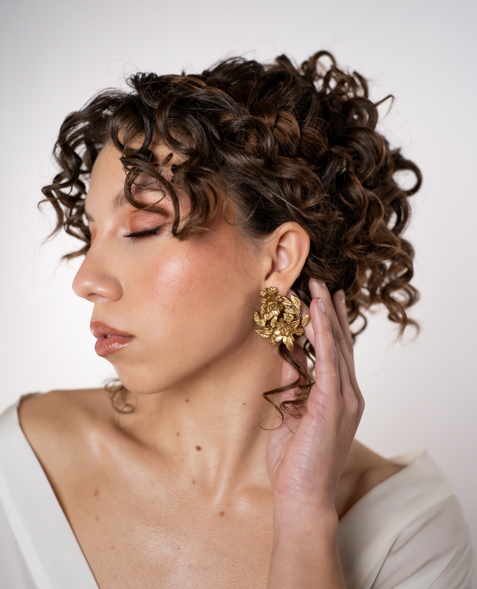 Bela III Brincos dourados florais usados por mulher com cabelo encaracolado e vestido branco