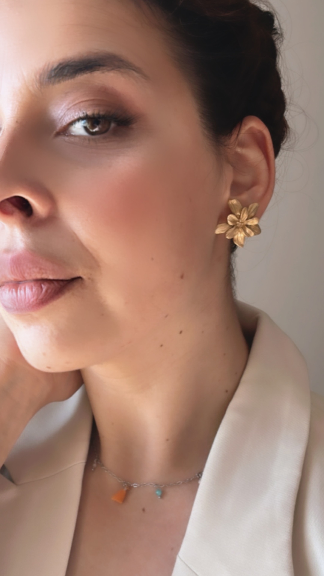 Mini Golden Flowers Brinco dourado em forma de flor usado por mulher com casaco bege claro e colar colorido