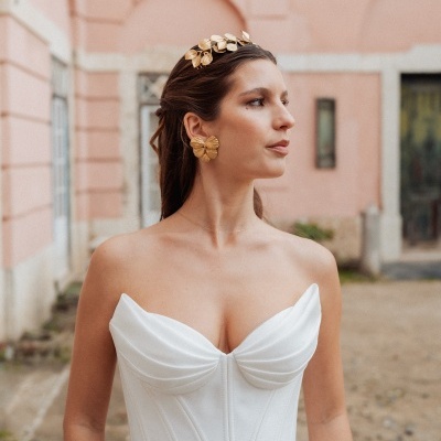 Mulher com vestido branco e acessórios dourados em ambiente exterior