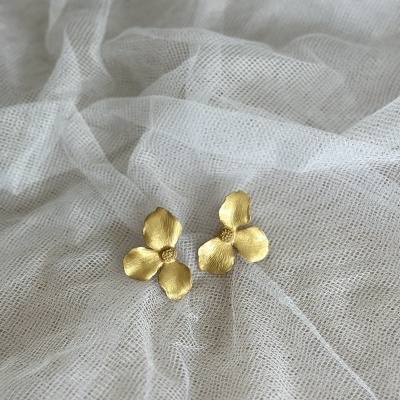 Brincos florais dourados sobre tecido branco translúcido