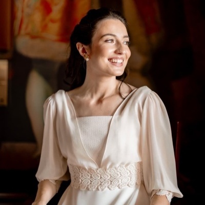 Mulher com vestido branco com renda na cintura e mangas compridas sentada sorrindo