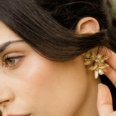 Brinco dourado de flores com pérola numa orelha feminina
