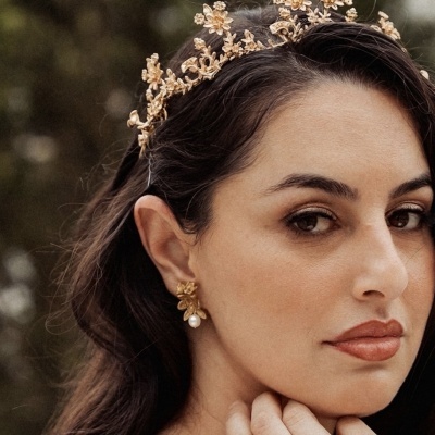 Mulher com tiara dourada floral e brincos dourados com pérola.