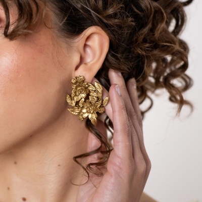 Brinco dourado floral em orelha feminina com cabelo cacheado.