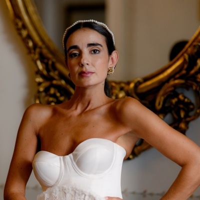 Mulher com vestido branco tipo corpete, fita de pérolas na cabeça e brincos dourados em interior elegante