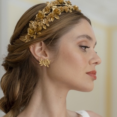 Mulher usando diadema e brincos dourados com design floral.