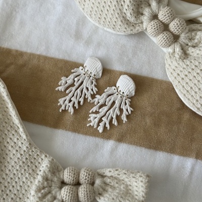 Biquíni de crochê branco com bola decorativa e brincos imitação coral sobre toalha de praia listrada em branco e bege