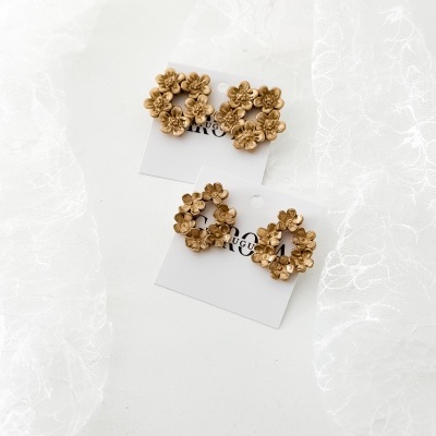Brincos dourados com flores em círculos em cartões brancos sobre fundo branco e renda.