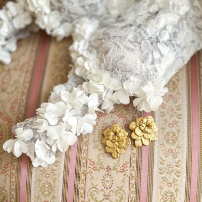 Soutien branco rendado com flores em tecido e brincos dourados sobre almofada listrada rosa e bege.