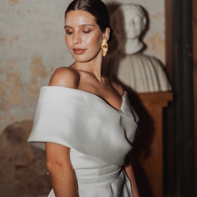 Mulher de vestido branco com ombro descoberto e brinco dourado