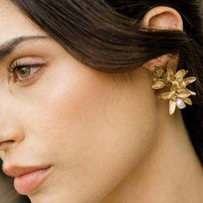 Perfil de mulher com brinco dourado floral e pérola