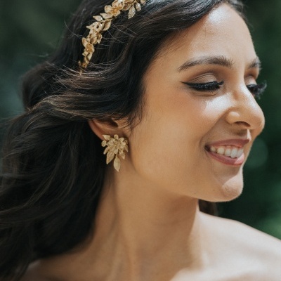 Diadema e brincos dourados com design de folhas em mulher sorridente de perfil