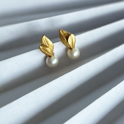 Brincos dourados com pérolas sobre superfície branca ondulada