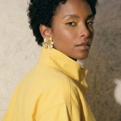 Mulher com camisa amarela e brincos dourados em forma de flor