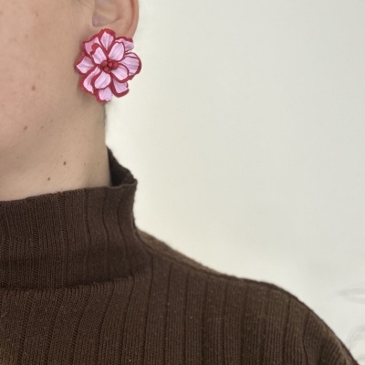 Brinco grande em forma de flor rosada com bordas vermelhas na orelha de uma pessoa
