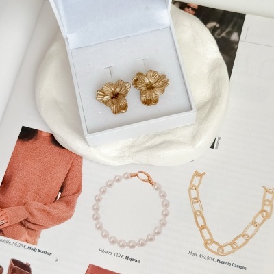 Brincos dourados em forma de flores numa caixa branca sobre revista aberta