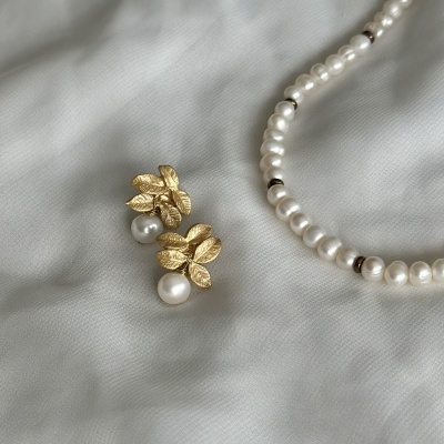 Colar e brincos de pérolas falsas com detalhes dourados em forma de folhas sobre tecido branco