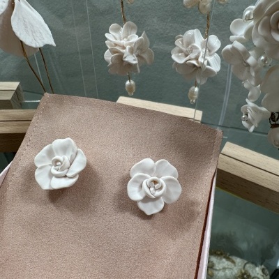 Brincos florais brancos sobre tecido rosa com acessórios brancos ao fundo