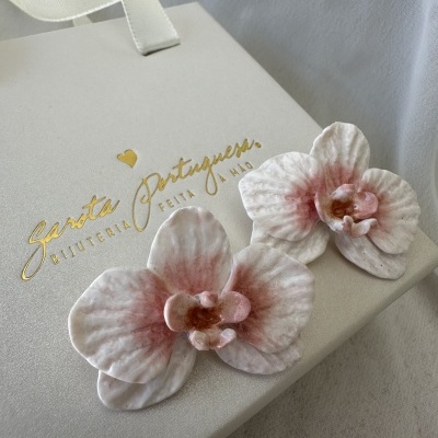 Flores artificiais brancas e rosas sobre caixa branca com texto dourado Garota Portuguesa