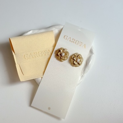 brincos flor dourada com centro branco em cartão GAROTA e embalagem amarela